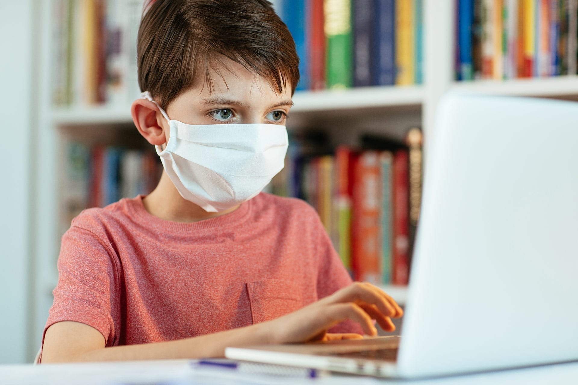 Boy wears a face respiratory face mask while working on schoolwork on his laptop