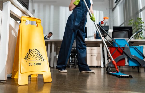 cropped view of cleaner washing floor with mop near wet floor caution sign